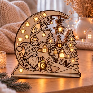 Op de afbeelding: Een halve maanvormige houten lichtdecoratie met een kabouter die een lantaarn vasthoudt, omringd door een winterdorp met dennenbomen, huisjes en een kerk. Het uitgesneden ontwerp wordt van binnenuit verlicht met warm licht.