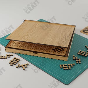 May include: A wooden puzzle box with a lid that opens to reveal a complex maze pattern. The puzzle pieces are scattered on a green mat.