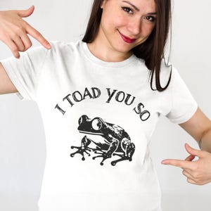 May include: White t-shirt with a black frog graphic and the text "I TOAD you so".
