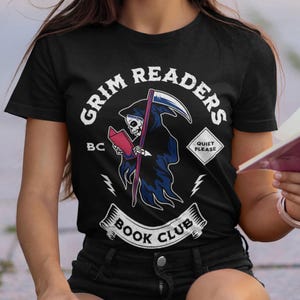 May include: Black t-shirt with a Grim Readers Book Club graphic featuring a skeleton in a hooded robe holding a book and a scythe. The graphic also includes the text "Grim Readers", "BC", "Quiet Please", and "Book Club".