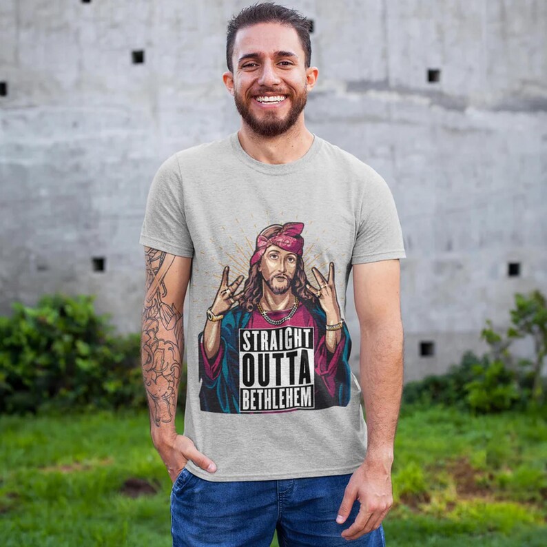 May include: A gray t-shirt with a graphic print of Jesus wearing a bandana and making a hand gesture. The text on the graphic says "Straight Outta Bethlehem".