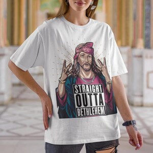 May include: White t-shirt with a graphic of Jesus wearing a bandana and a gold chain. The graphic says "Straight Outta Bethlehem".