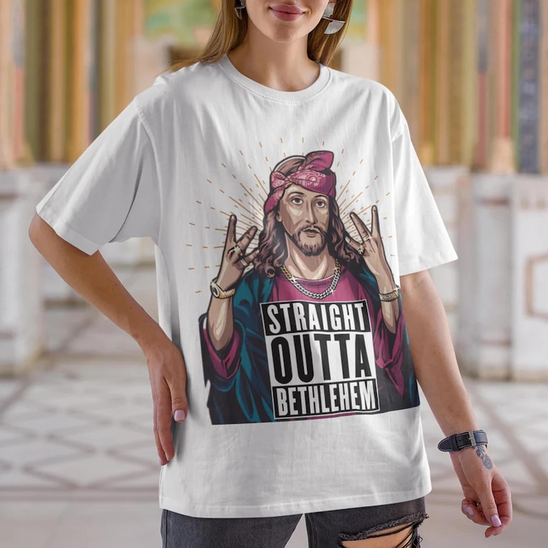 May include: White t-shirt with a graphic of Jesus wearing a bandana and a gold chain. The graphic says "Straight Outta Bethlehem".