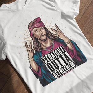 May include: White t-shirt with a graphic of Jesus wearing a bandana and a gold chain. The graphic says "Straight Outta Bethlehem".