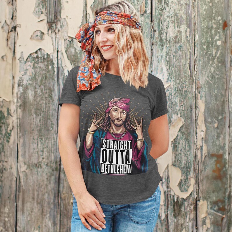 May include: A heather grey t-shirt with a graphic of Jesus wearing a bandana and making a gang sign. The text on the shirt reads "Straight Outta Bethlehem".