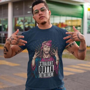 May include: A navy blue t-shirt with a graphic of Jesus wearing a bandana and a gold chain. The graphic has the text "Straight Outta Bethlehem" in a white box.