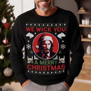 Könnte beinhalten: Schwarzer Weihnachtspullover mit einem roten und weißen Schneeflockenmuster. Der Pullover zeigt ein Porträt von John Wick mit einem Weihnachtsmann-Hut und dem Text "We Wick You A Merry Christmas".