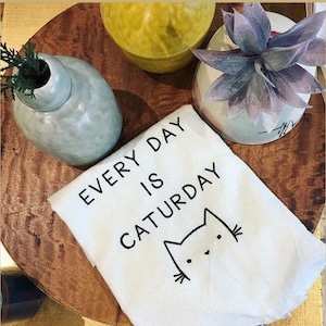 May include: White kitchen towel with black text that reads "Every day is Caturday" and a black line drawing of a cat's face.