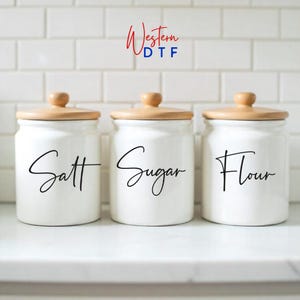 May include: Three white ceramic kitchen canisters with wooden lids. The canisters are labeled "Salt", "Sugar", and "Flour" in black script. The logo "Western DTF" is in the top center.