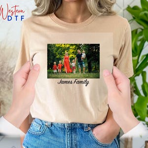 May include: A tan t-shirt with a photo of a family of five standing in a park. The photo is surrounded by a white border and the text "James Family" is printed below the photo.