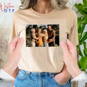 May include: A beige t-shirt with a photo of a family of six standing in a forest. The family is smiling and looking at the camera. The photo is printed in the center of the shirt.