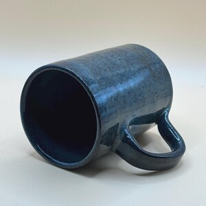 May include: A handmade ceramic mug with a dark blue glaze. The mug has a cylindrical shape with a rounded handle. The interior is a darker shade of blue. The mug is approximately 10 cm tall and 8 cm in diameter.