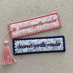 Puede incluir: Dos marcapáginas bordados con el texto « dearest gentle reader ». Uno es rosa con un estampado floral y una borla rosa. El otro es azul con un estampado floral.