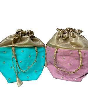 May include: Two drawstring bags. One is turquoise with gold accents and the other is pink with gold accents. Both bags have a gold satin top and a gold drawstring closure. The bags are decorated with small, gold floral embellishments.