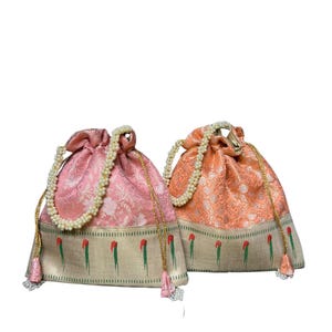 May include: Two drawstring bags. One is pink with a floral pattern, the other is peach. Both have a pearl-beaded handle and a decorative border with red and green accents. The bags are made of a shiny fabric.