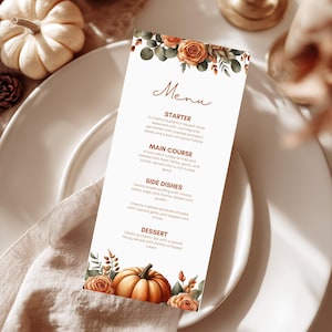 May include: A menu card with floral and pumpkin illustrations. The card features the word "Menu" in elegant script. The menu lists a starter, main course, side dishes, and dessert. The card is placed on a white plate with a linen napkin.