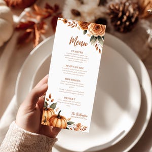 K&ouml;nnte beinhalten: Eine Men&uuml;karte mit Herbstthema, mit Aquarellk&uuml;rbissen und floralen Akzenten. Die Speisekarte enth&auml;lt Abschnitte f&uuml;r Vorspeise, Hauptgericht, Beilagen und Dessert. Der Text lautet "Menu" in eleganter Schrift.
