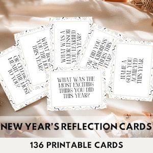 Puede incluir: Un conjunto de tarjetas de reflexión de Año Nuevo con preguntas como "¿Qué fue lo más emocionante que hiciste este año?" y "Nombra una meta que lograste este año". Las tarjetas son blancas con texto negro y detalles dorados. La imagen también incluye el texto "136 Printable Cards."
