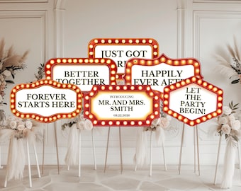 Könnte beinhalten: Eine Sammlung von sechs rechteckigen und sechseckigen Schildern im Festzelt-Stil mit roten Rändern und beleuchteten Glühbirnen. Die Schilder zeigen schwarzen Text, darunter "JUST GOT MARRIED", "BETTER TOGETHER", "HAPPILY EVER AFTER", "FOREVER STARTS HERE", "INTRODUCING MR. AND MRS. SMITH 08.22.2026" und "LET THE PARTY BEGIN!"