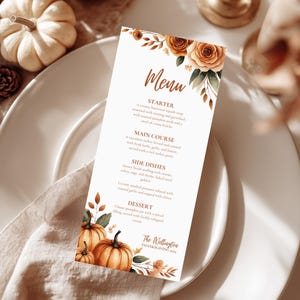 May include: A Thanksgiving menu card with floral and pumpkin illustrations. The menu features a starter, main course, side dishes, and dessert. The menu is on a white plate with a linen napkin and pumpkins.