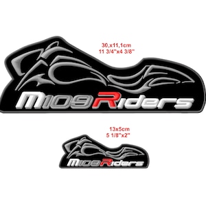 May include: Two black and white decals with the text "M109 Riders". The larger decal measures 11 3/4" x 4 3/8" (30 x 11.1 cm), and the smaller one is 5 1/8" x 2" (13 x 5 cm). The word "Riders" is in red.
