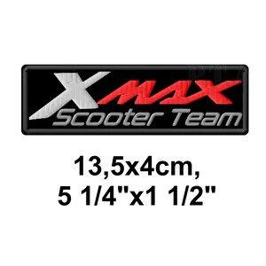 以下が含まれることがあります： 黒い長方形の背景に、白、赤、グレーで「X-MAX Scooter Team」の文字が刺繍されたパッチ。サイズは13.5 x 4cmです。
