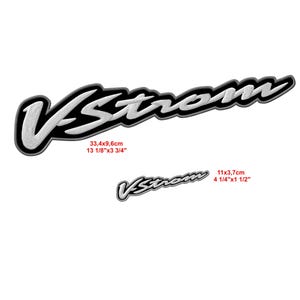 Könnte beinhalten: Zwei schwarz-weiße V-Strom Logo-Aufkleber. Der größere Aufkleber misst 33,4 x 9,6 cm (13 1/8" x 3 3/4"), der kleinere 11 x 3,7 cm (4 1/4" x 1 1/2"). Der Text ist in einer stilisierten Schrift mit weißer Umrandung.