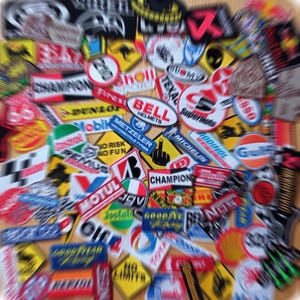 Può includere: Una collezione di toppe colorate con vari marchi e loghi, tra cui Michelin, Bell Helmets, Champion, Texal e Mobil. Le toppe sono principalmente rosse, gialle, blu e bianche.