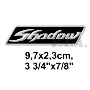 May include: A rectangular patch with the word "Shadow" in white, stylized lettering. The patch has a black background and a white border. The patch measures 3 3/4" x 7/8".