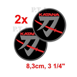 May include: Two embroidered patches with a black circular background. Each patch features the word "KATANA" in red, a gray stylized sword design, and a red katana. The patches are 3 1/4 inches in diameter.