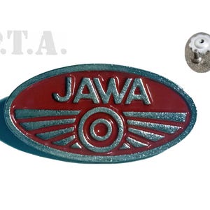 May include: A red and silver oval-shaped pin with the word "JAWA" in silver lettering and a silver circle with a red center. The pin has a silver wing design on either side of the circle.