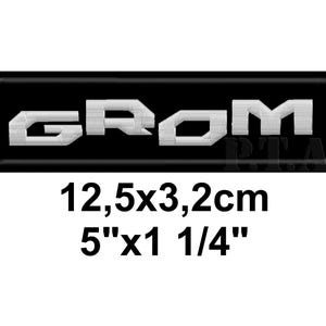 Op de afbeelding: Geborduurde patch met het woord "GROM" in witte blokletters op een zwarte rechthoekige achtergrond. De patch meet 12,5 cm x 3,2 cm.