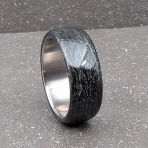 May include: A black and silver ring with a textured finish. The ring is made of titanium and has a wide band.
