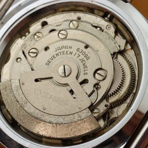 May include: Close-up of a vintage watch movement, showcasing intricate gears, screws, and the Seiko logo. The mechanism is labeled "Japan Seventeen 17 Jewels 6309A". The watch case is silver-toned.
