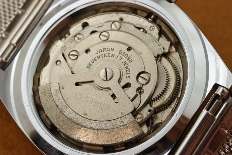 May include: Close-up of a vintage watch movement, showcasing intricate gears, screws, and the Seiko logo. The mechanism is labeled "Japan Seventeen 17 Jewels 6309A". The watch case is silver-toned.