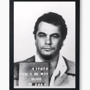 May include: Black and white mugshot of a man with short dark hair. The mugshot is framed in black and includes a New York City Police Department ID card with the number 417073.