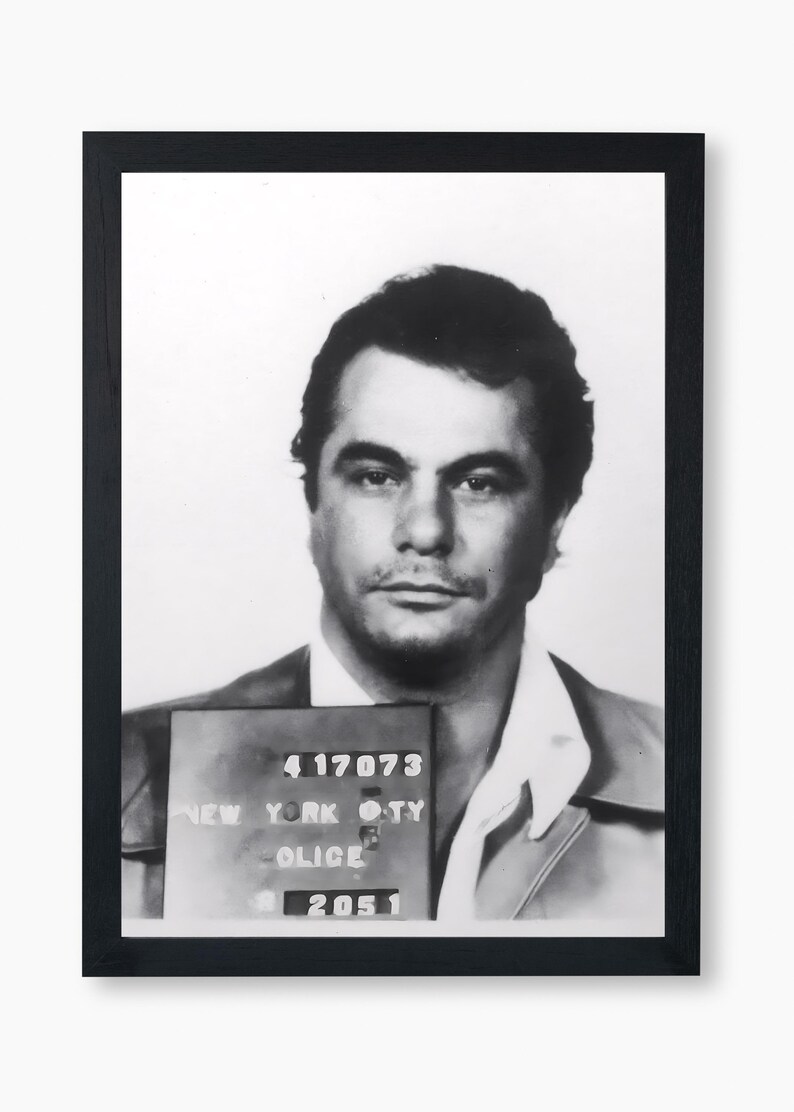 May include: Black and white mugshot of a man with short dark hair. The mugshot is framed in black and includes a New York City Police Department ID card with the number 417073.