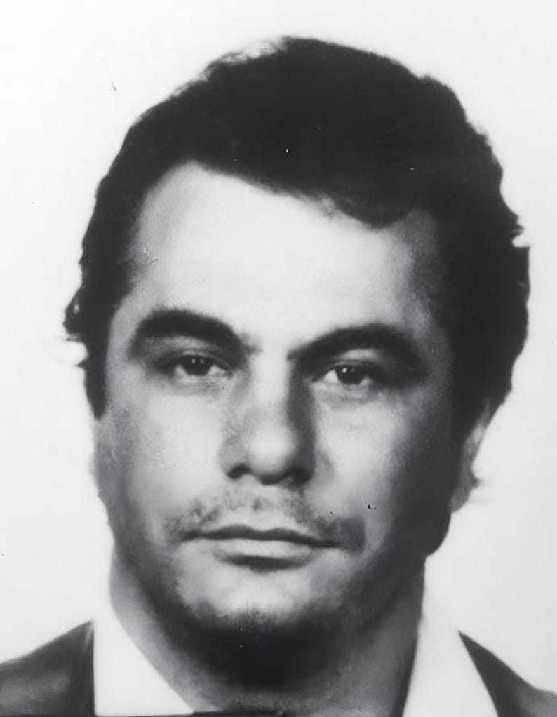 May include: Black and white mugshot of a man with short dark hair. He is looking directly at the camera with a serious expression.