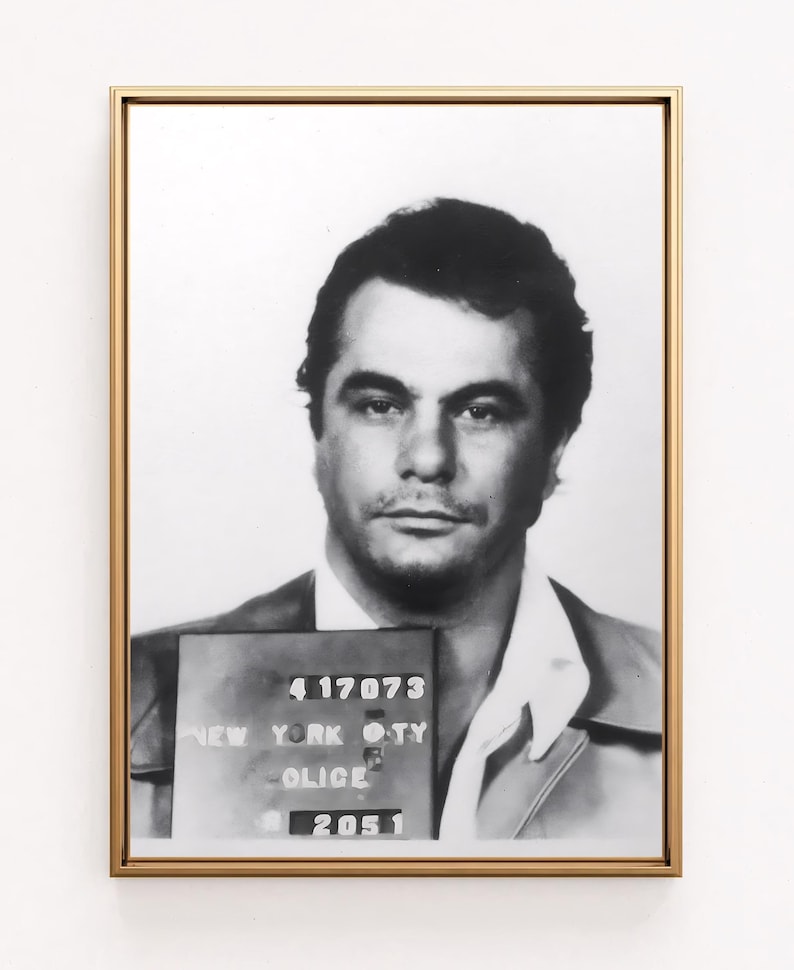 May include: Black and white mugshot of a man with short dark hair. The mugshot is framed in gold and has the text "417073 NEW YORK CITY POLICE 2051" on a white background.