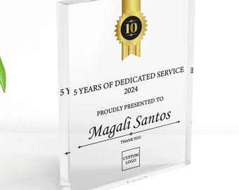 Op de afbeelding: Een heldere acryl prijs met gouden details. De tekst luidt "5 jaar toegewijde service 2024" en "Met trots gepresenteerd aan Magali Santos". Een gouden zegel met het nummer "10" staat bovenaan.
