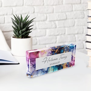 May include: A colorful acrylic desk nameplate with a white background and the text "Helena Terry, Journalist". The background features abstract swirls of pink, purple, blue, and gold.
