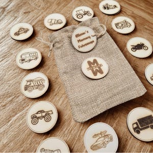 Pode incluir: Jogo da memória em madeira com ilustrações de veículos, incluindo um carro, um camião e um autocarro. O jogo inclui um saco com cordão e fichas de madeira com o texto "Elmer's Memory Fahrzeuge" e "Memory".