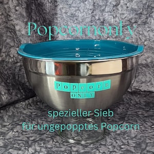 Puede incluir: Un bol de palomitas de acero inoxidable con interior y borde turquesa. Las palabras "Popcorn only" se muestran en la parte delantera. El bol está diseñado para palomitas sin reventar y se apoya en una base de cristal transparente.