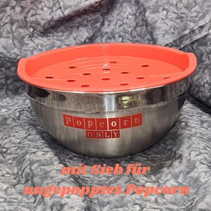 May include: A stainless steel bowl with a red lid and a strainer. The bowl has the words "Popcorn Only" printed on the side. The lid has holes for steam to escape.