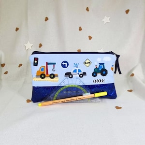 May include: A blue pencil case with a zipper closure. The front of the case features a light blue background with a variety of colorful vehicles, including a truck, a police car, and a tractor. The text "SLOW" is also visible on the case. The case is lined with a blue glitter fabric. A yellow pencil, a protractor, and a ruler are visible in front of the case.