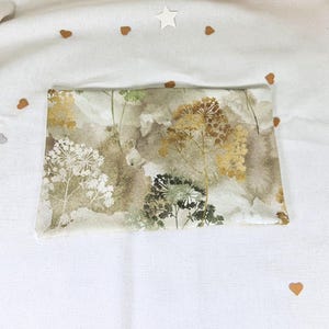 May include: A beige fabric with a watercolour print of brown, green and gold wildflowers. The fabric has a subtle texture.
