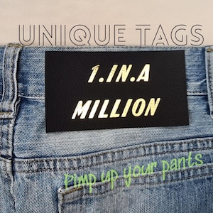 Könnte beinhalten: Ein schwarzer Leder-Patch mit goldener Aufschrift "1.IN.A MILLION" auf einer blauen Jeans. Der Text "Pimp up your pants" ist in Grün unter dem Patch geschrieben.