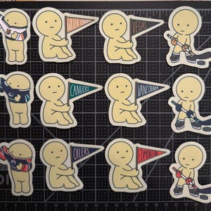 May include: A collection of twelve die-cut stickers featuring a pale yellow cartoon character in various hockey-themed poses, including holding pennants labeled Golden Knights, Vegas, Canucks, Vancouver, Oilers, and Edmonton, or playing with a hockey stick.