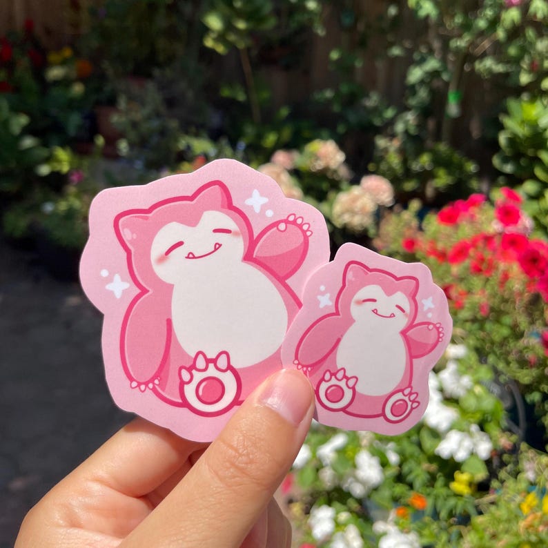 May include: Two pink cartoon stickers of a pink Pokemon character with a big smile and a paw print on its belly. The stickers are on a white background.