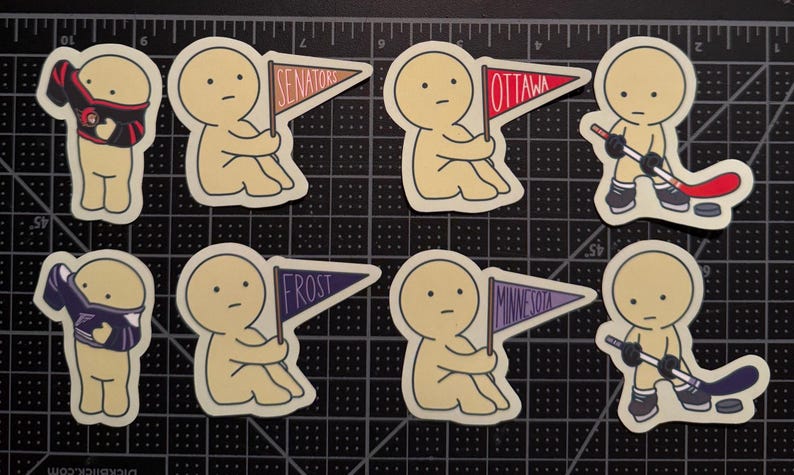 May include: A set of eight die-cut stickers featuring cartoon figures in various poses. Some figures hold pennants labeled Senators, Ottawa, Frost, or Minnesota, while others wear jerseys or hold hockey sticks with pucks on a black grid cutting mat.